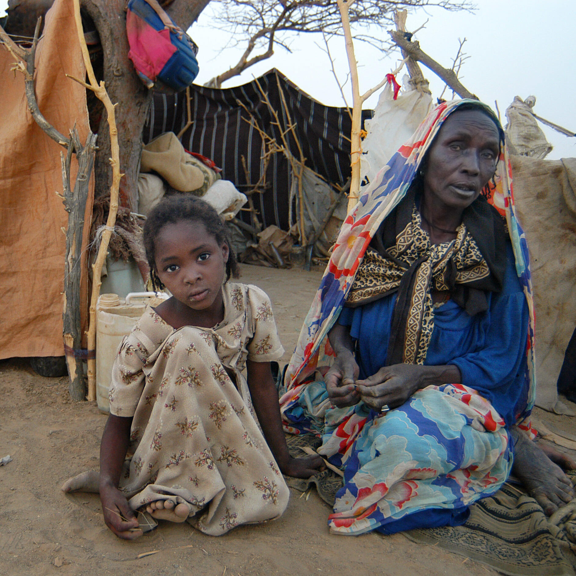 Sudanese refugee woman and girl sitting outside a shelter made of blankets and sheets.