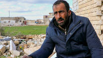 A Syrian man, Faisal (not his real name), stands outside in the cold with rubble behind him after the Feb. 6, 2023 earthquake.