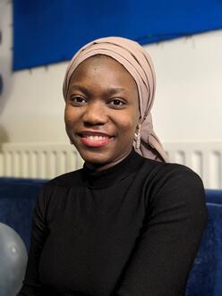 Fatou Jeng smiles at the camera infront of white and blue background