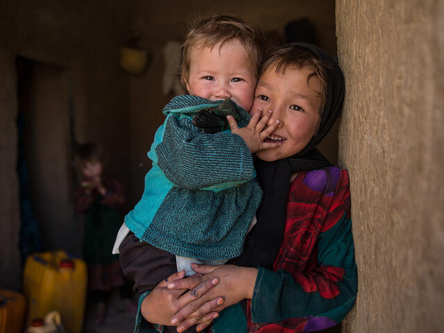 A young girl holds her younger sibling. 