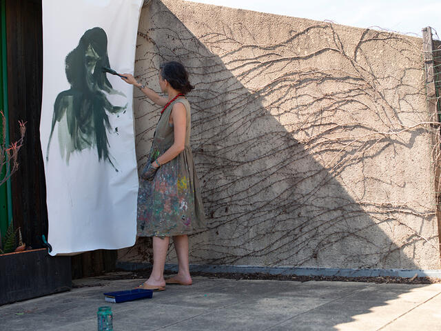 Diala outside painting a large image of a green woman.