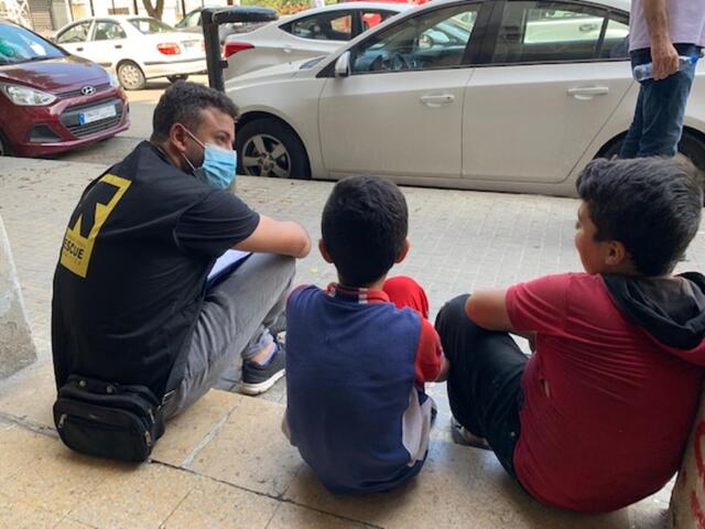 An IRC staff member sits on the pavement with two young boys in Beirut.