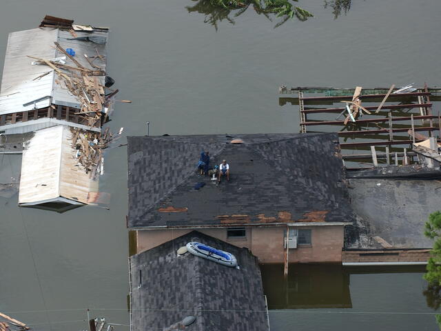 People sit on a roof in a flooded New Orleans neighborhood waiting to be rescued after Hurricane Katrin