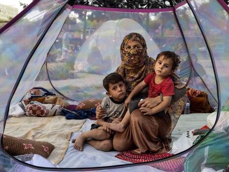 An Afghan woman and two young children sitting on the floor of a tent.