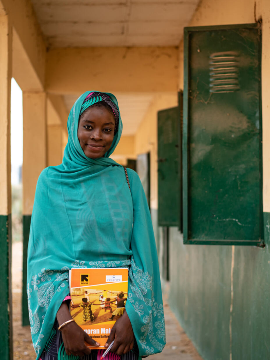 Teacher Aisha holding books outside school.