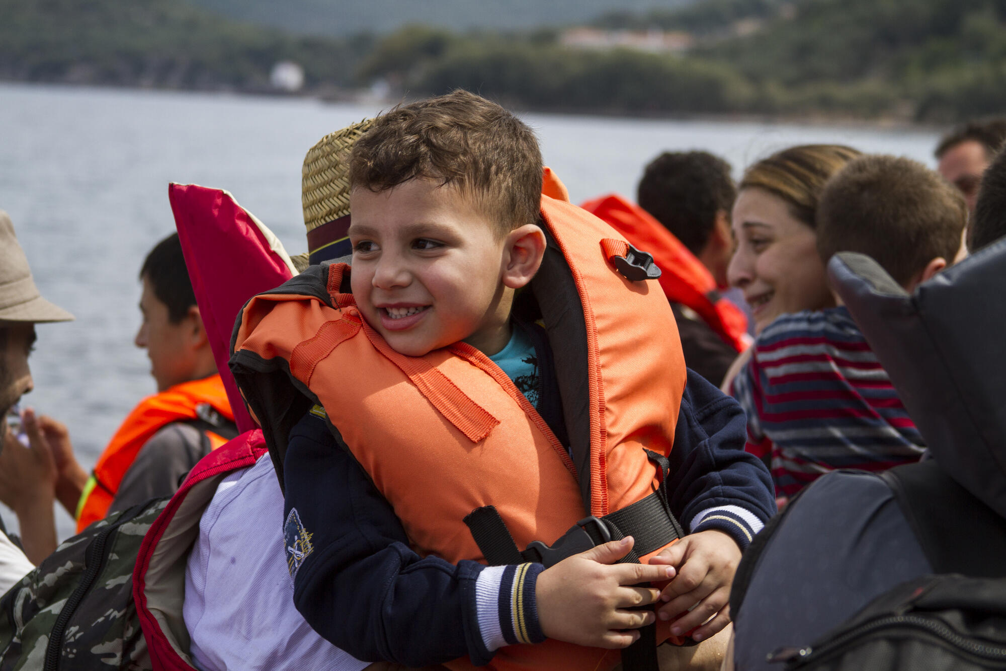 A small boy wearing a life vest nears the Greek coast in a rubber raft overflowing with other refugees.