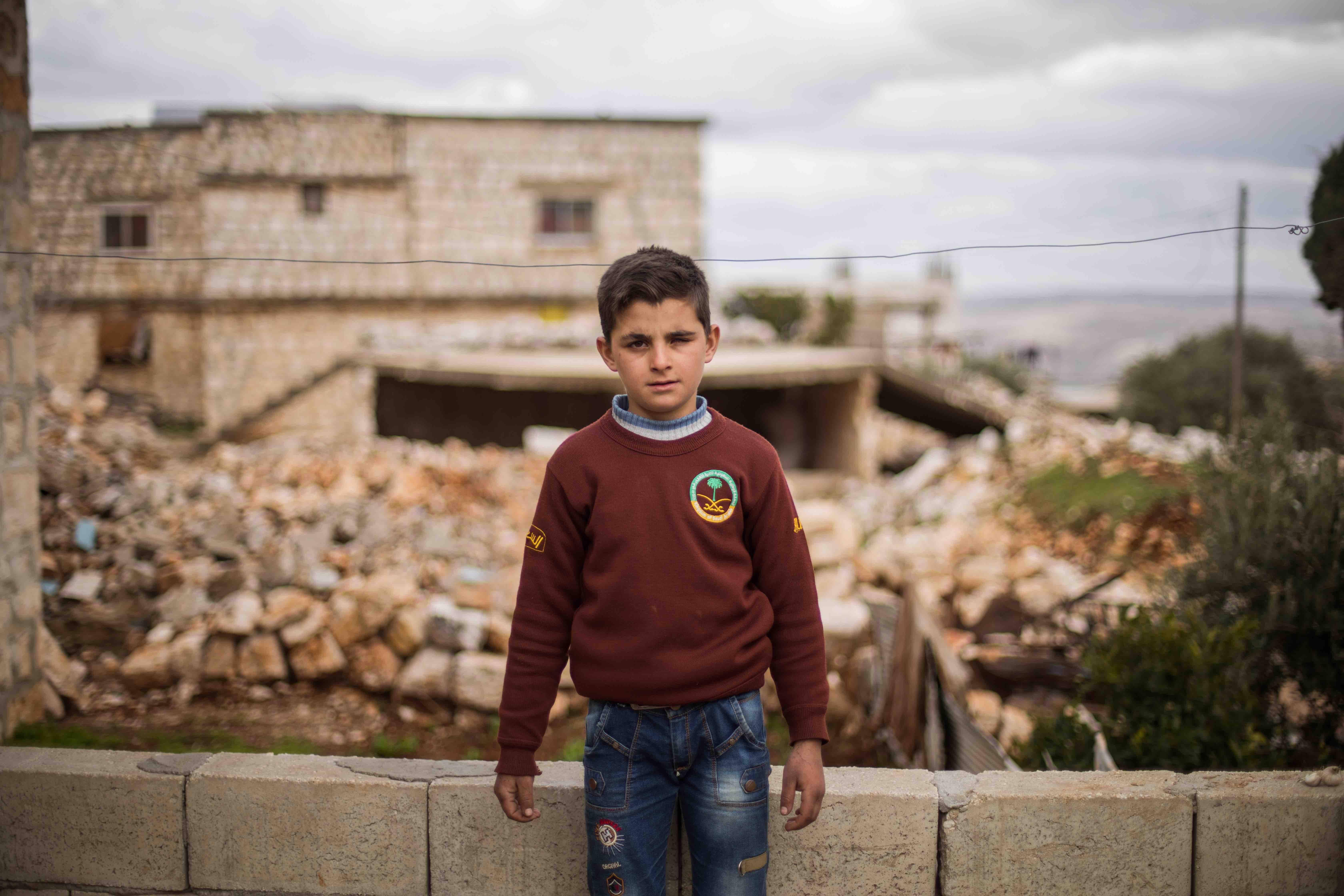 Ten-year-old Ali stands in front of his family's home which was damaged by an airstrike. 