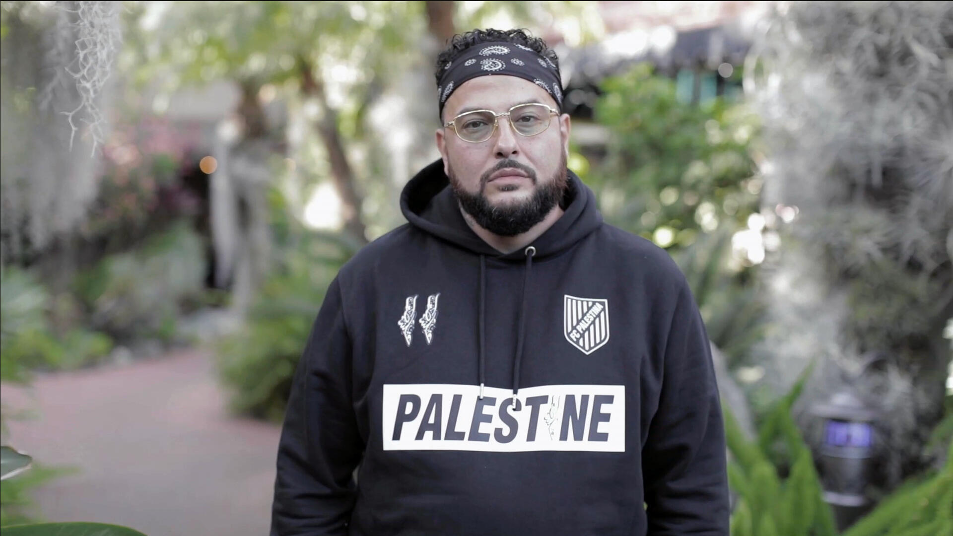 Rapper Belly stares into the camera. He is wearing a Palestine hoodie.