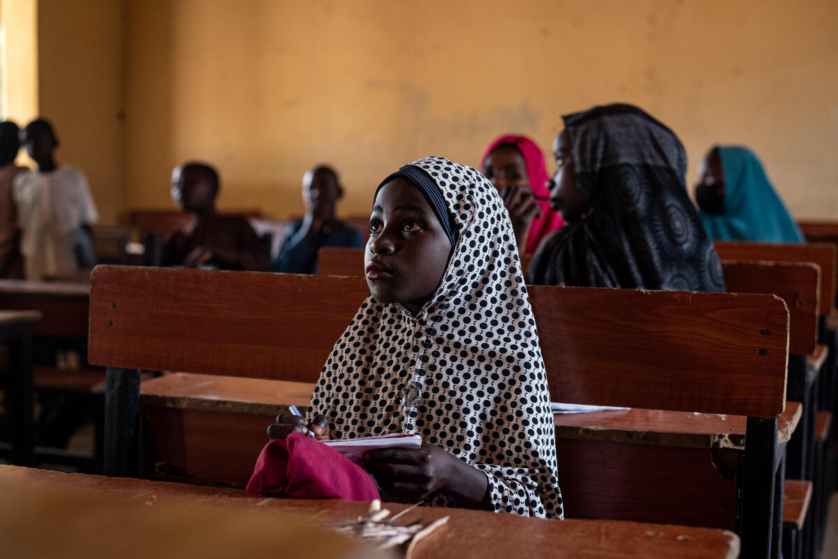 Young Fatima sits in a class room looking up towards where the teacher stands. 