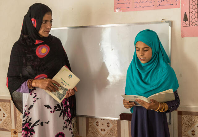 A teacher looks on as a young girl reads to the class