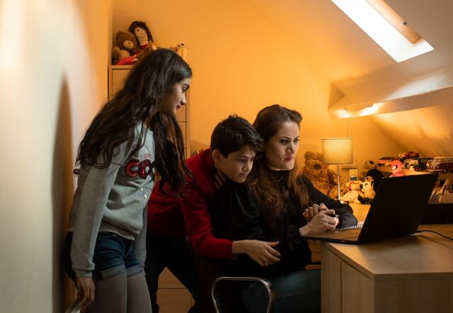 A woman sitting at a desk in front of a laptop, and two children standing next to her