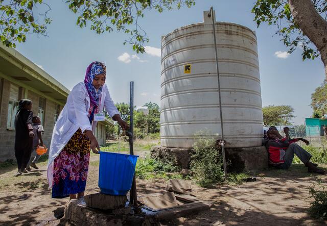 A woman holds out a bucket under a running tap to collect water