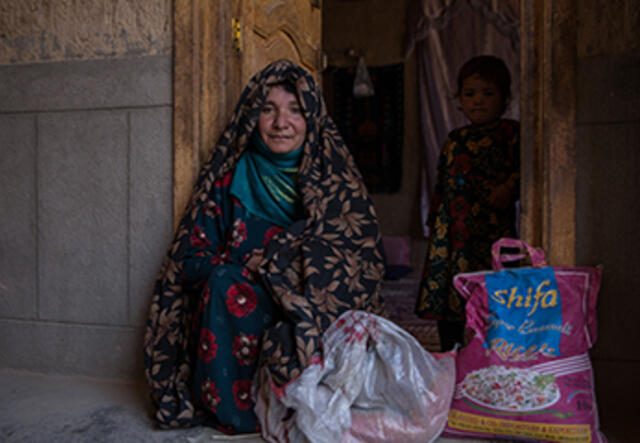 Woman in Afghanistan sits outside her home with a sack of rice.