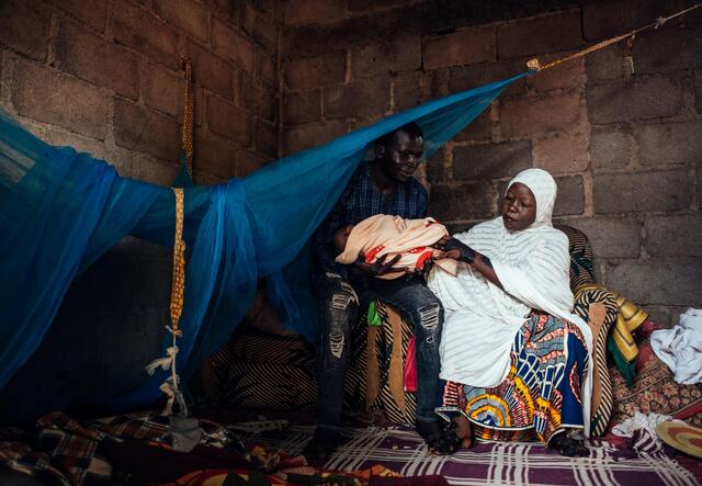 A young couple, Hussaini and Ibrahim, sitting on a chair with their newborn baby