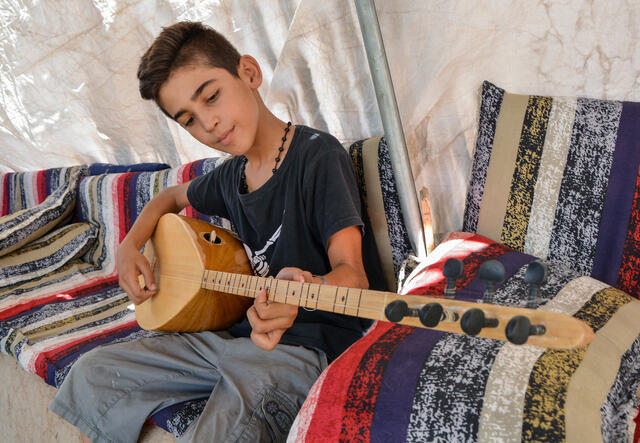 Yasser plays his buzuq in his family's tent in a displacement camp in northeast Syria.